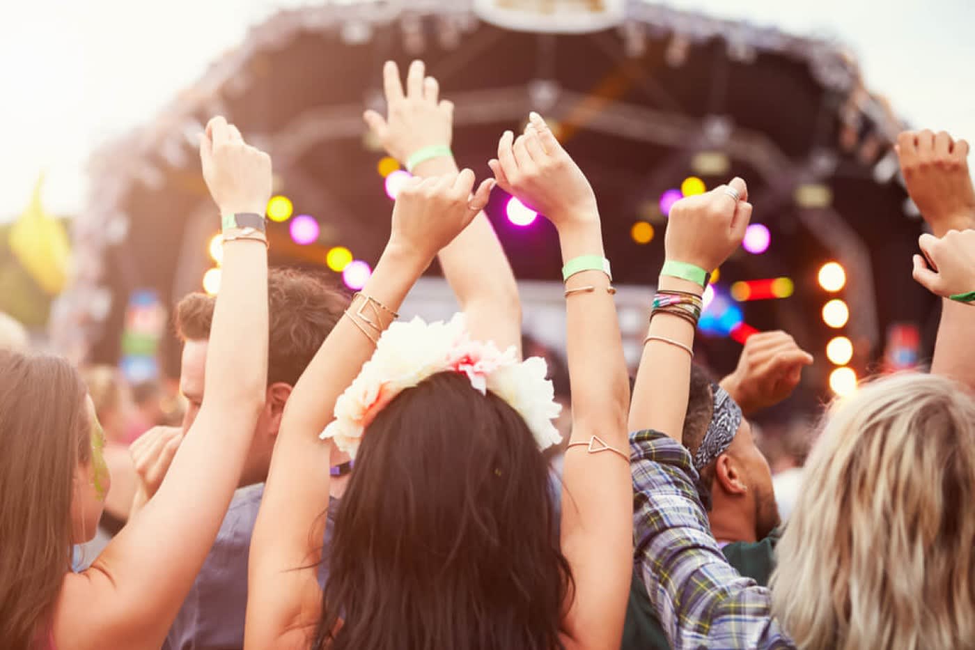 A group of women standing with their arms up and dancing at a live music festival at an outdoor venue