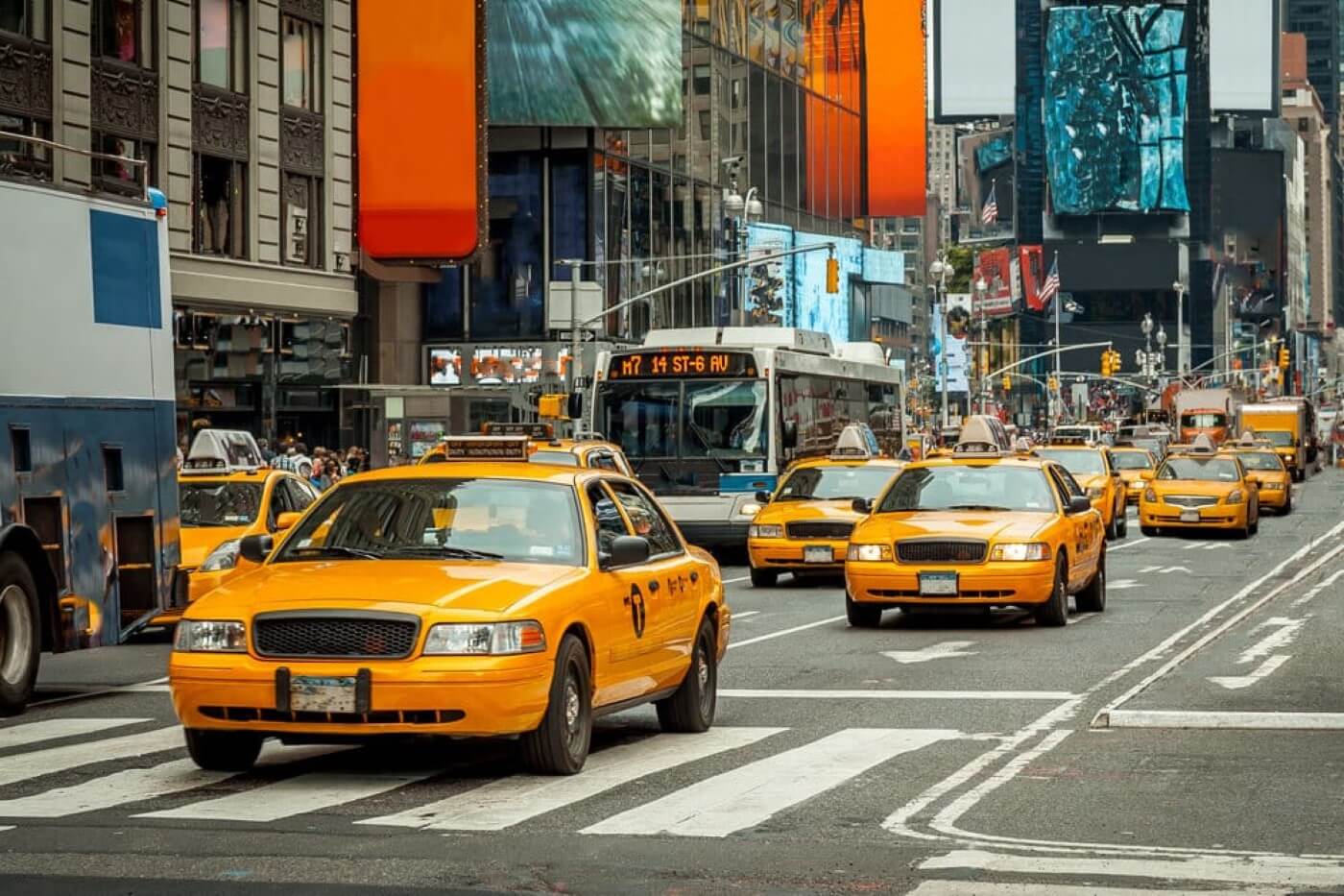A busy road in New York City with lots of yellow taxis driving down next to a large bus