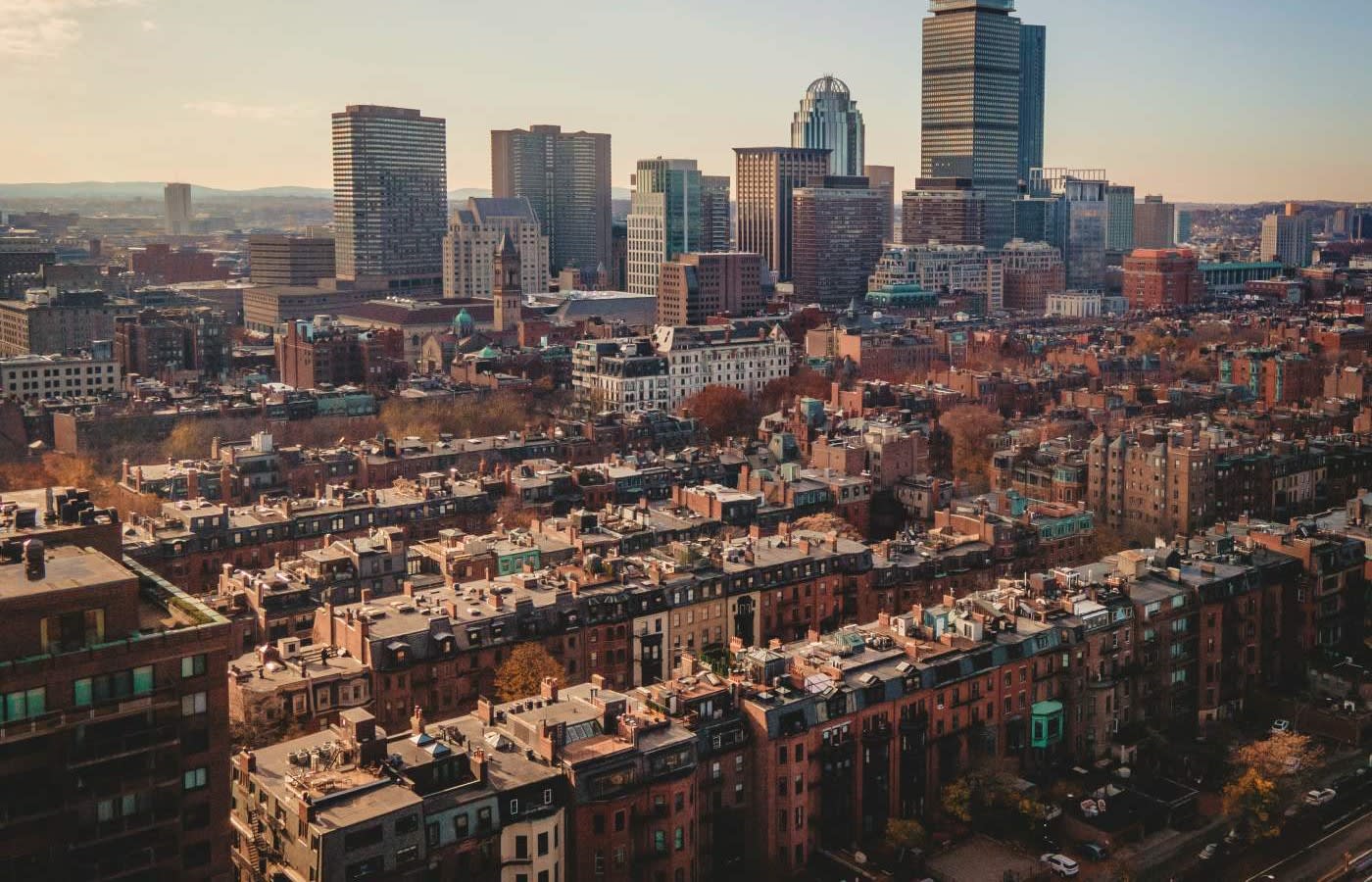 Aerial view of the back bay neighborhood of boston. Several rows of brownstone buildings visible in the foreground with the city skyline behind.