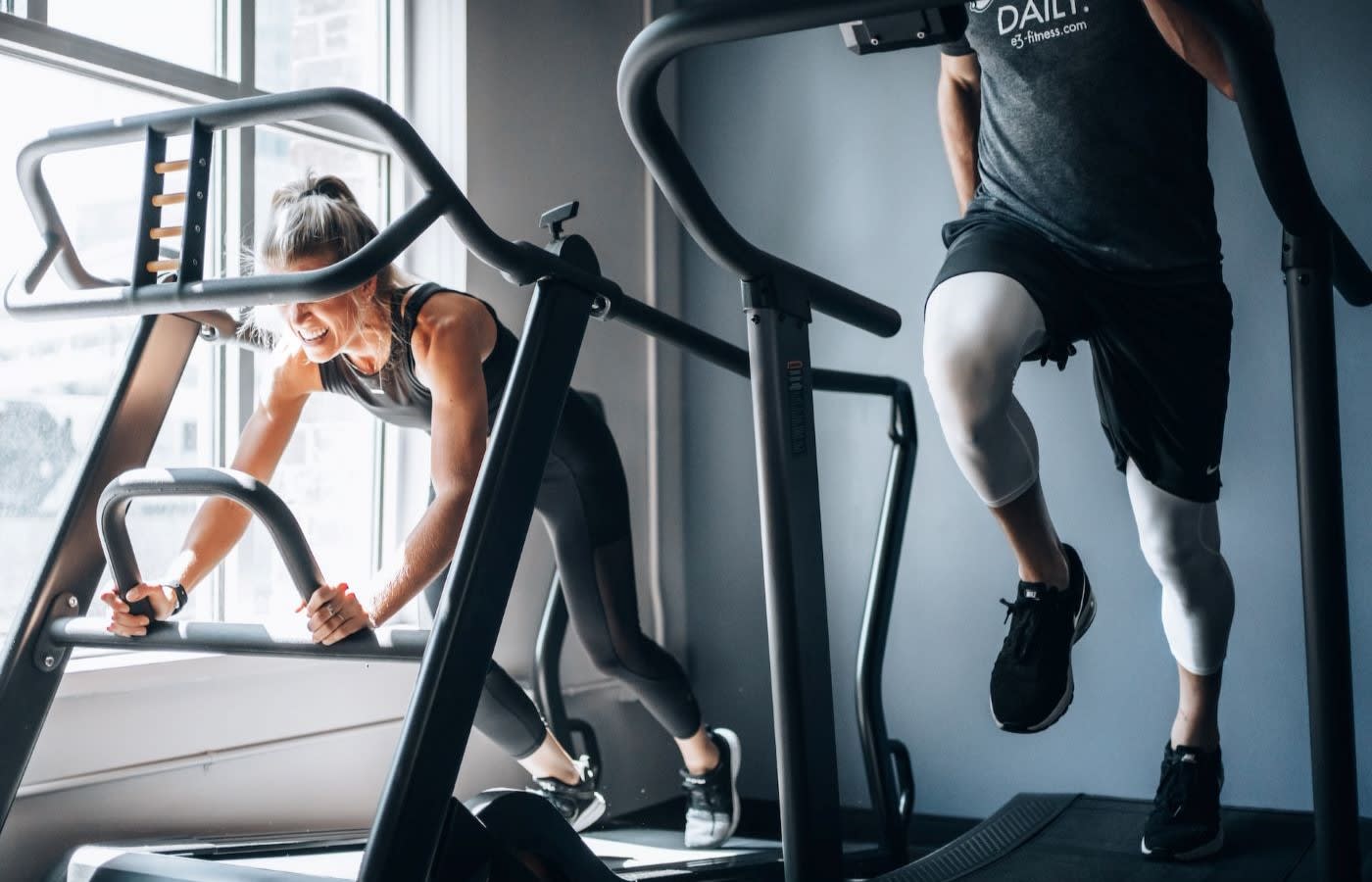 A man and a woman each running on a treadmill in a gym.