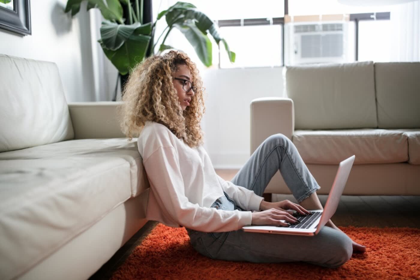 housing in DC woman sitting on floor with back to couch searching for apartments on laptop