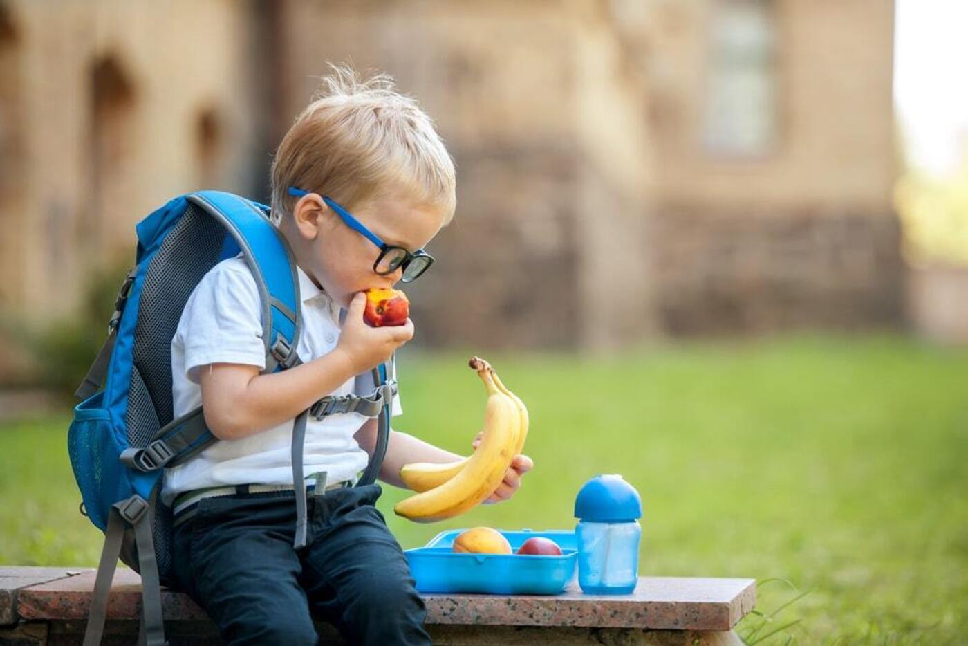 international schools Boston boy wearing glasses eating apple and looking at banana