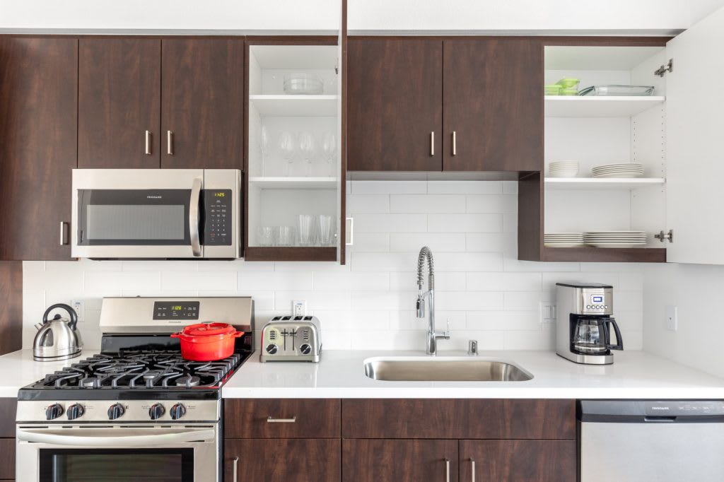A fully equipped kitchen with dark wood cabinets and plates and cups on each shelf. There is a red pot on the stove and a white coffee maker on the counter