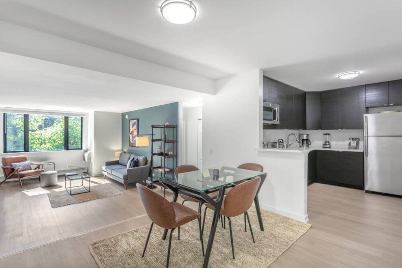 a large open plan living room with a dining area and an open kitchen. The dining table is in the center with four chairs all around and the kitchen is off to the right hand side