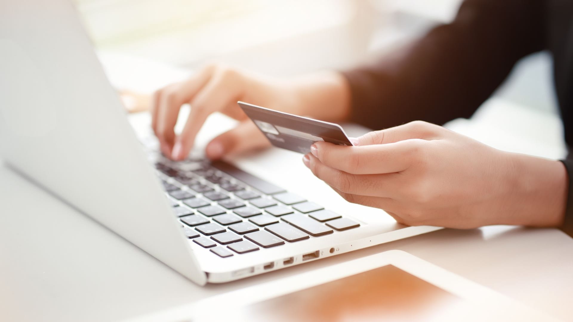 person holding credit card implying online payment with white laptop