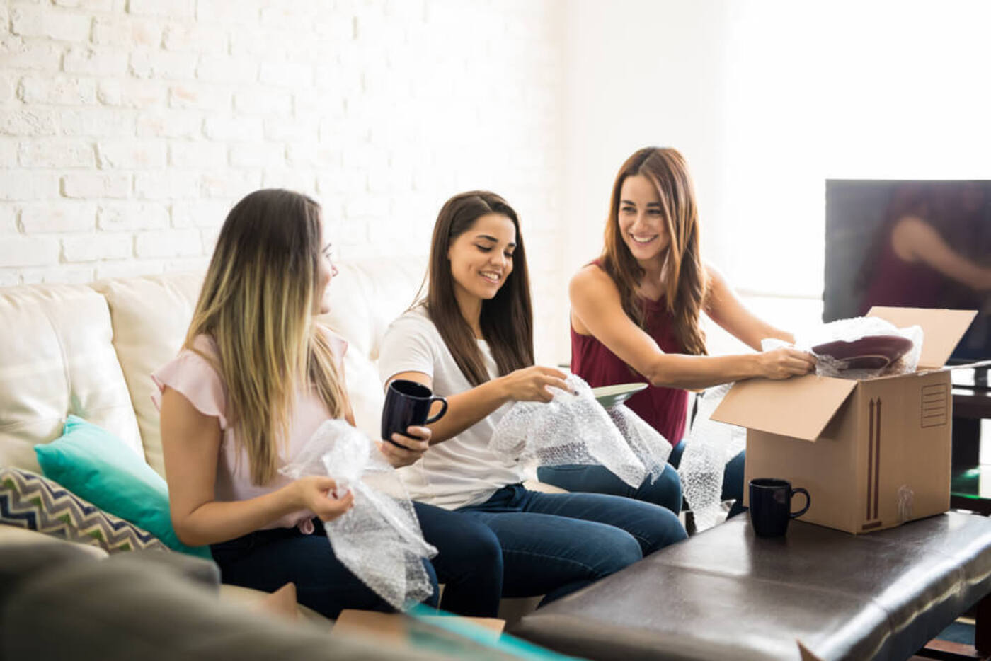 three girls who are roommates sitting on a couch unpacking their belongings