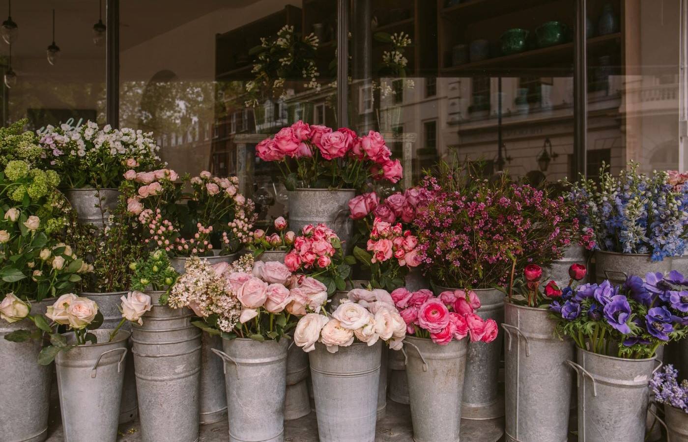A row of different flowers in tall steel buckets.