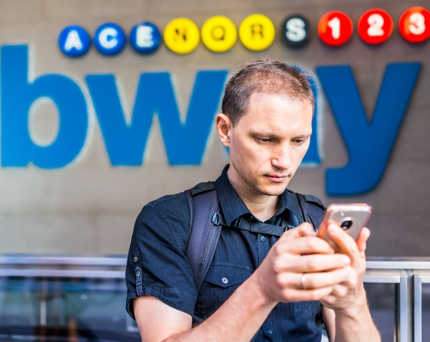 young caucasian man looking down at smartphone by subway metro in NYC