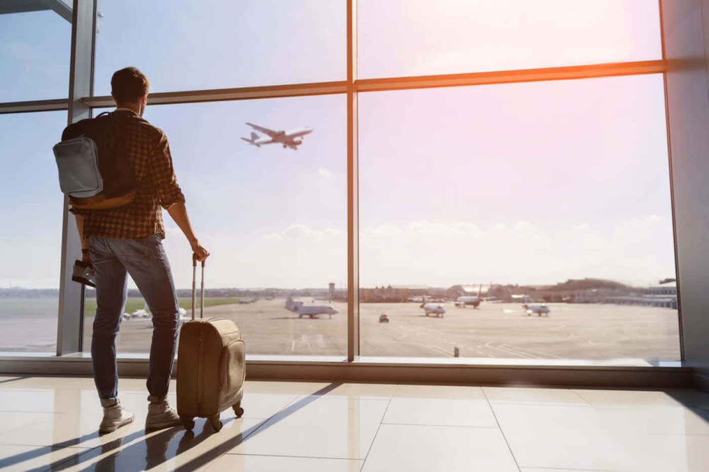 man stands at the airport looking out the window while holding his suitcase and staring at the plane fly by