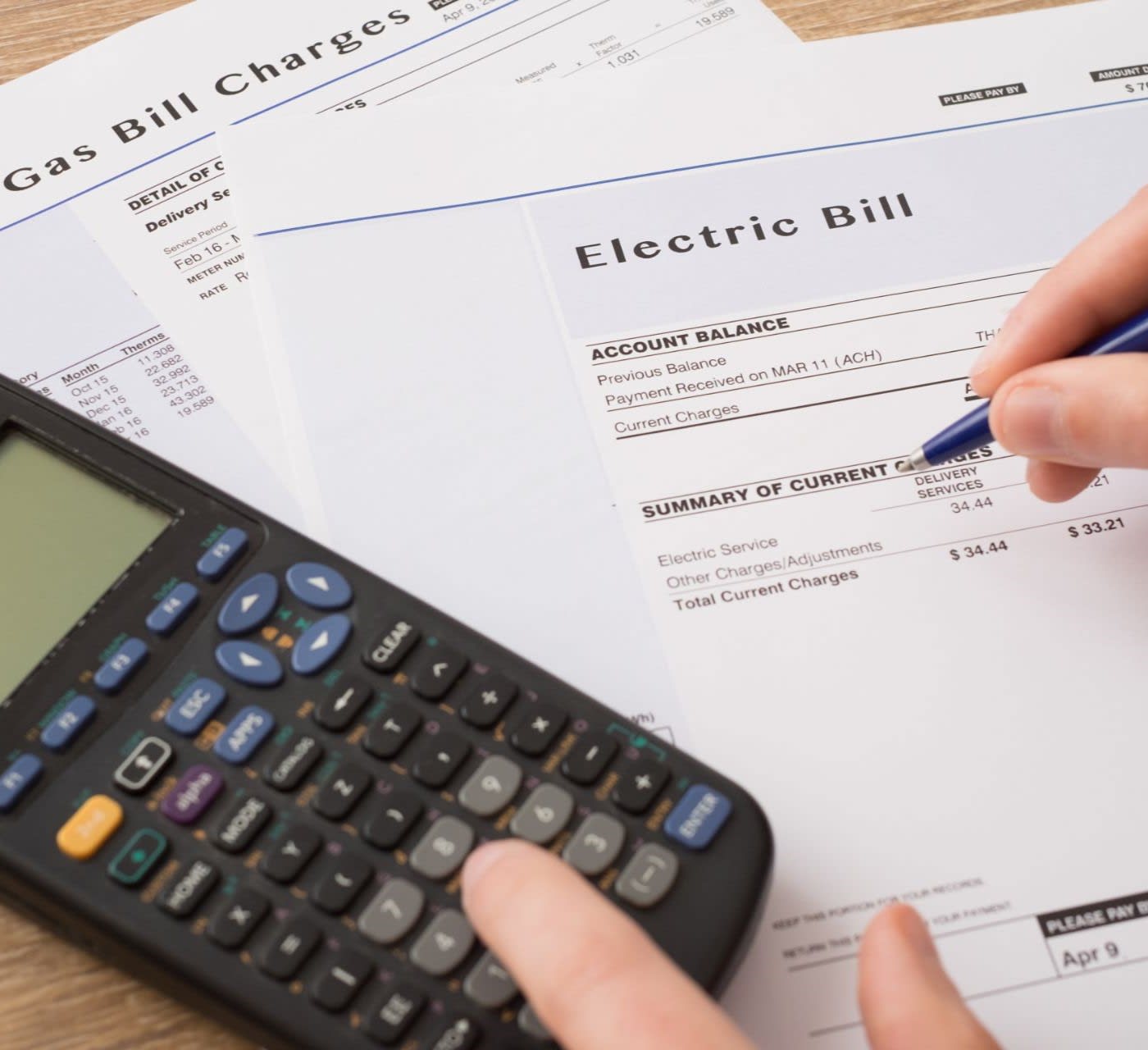 utility bill charges paper form on table with person holding onto calculator and pen