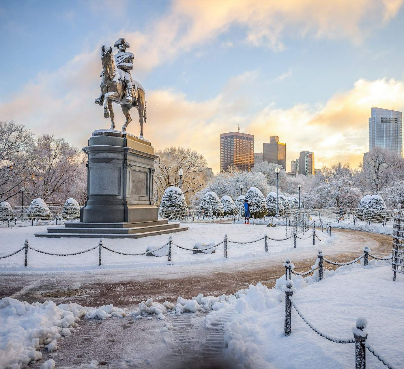 George Washington statue in the middle of Boston Public garden. It's snowy but the sky is blue with golden clouds closing in on the sunset.