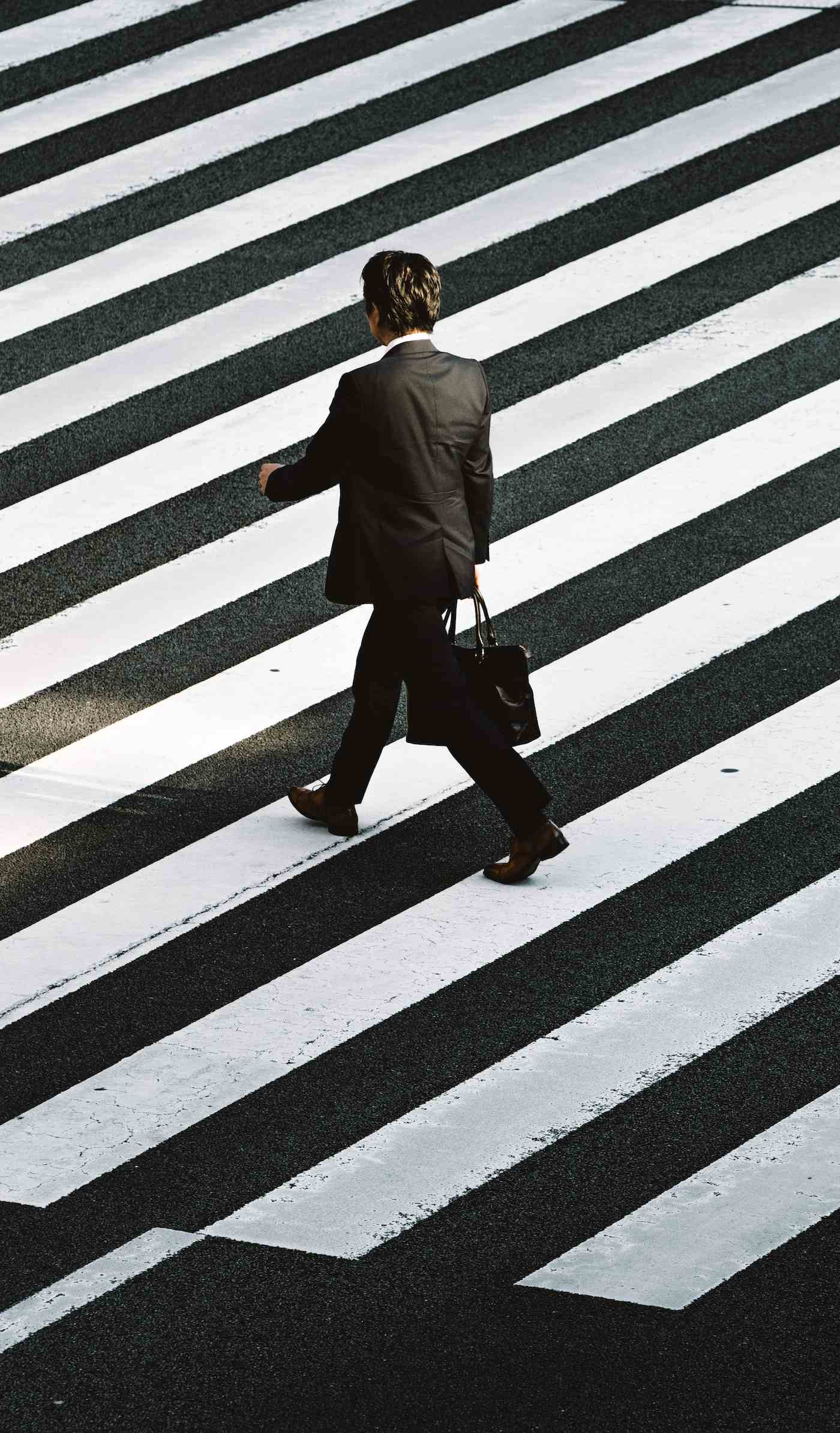 man dressed professionally walking on a crosswalk on the street holding a briefcase