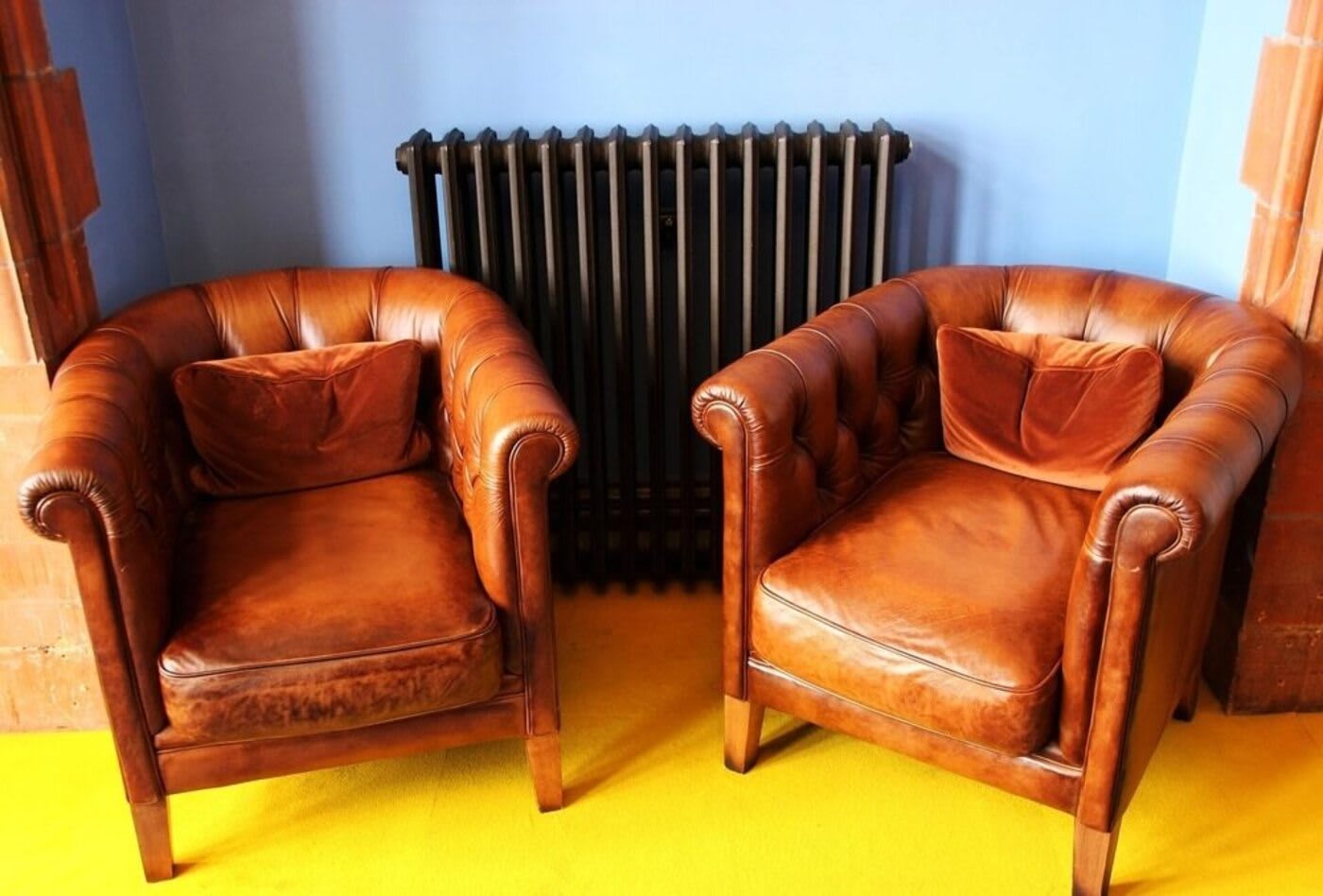 two empty brown leather chairs and sitting in front of a heater and a blue painted wall on a yellow painted floor