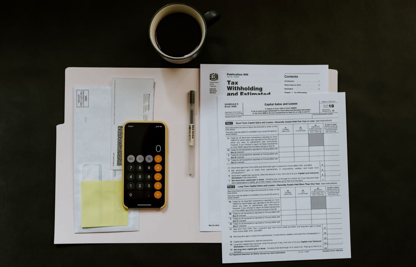 A black desk with tax forms, a cup of coffee and a smartphone.