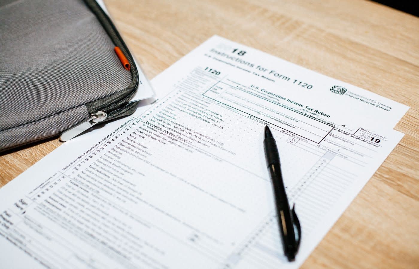 A tax form on a wooden desk with a black pen on top of it.