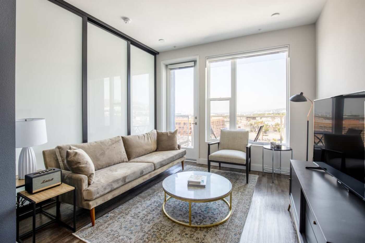 modern living room with lots of natural light, gold and dark wood tones and a round marble coffee table