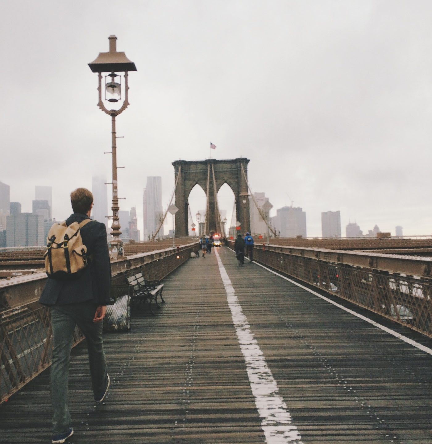 man professionally dressed wearing backpack, crossing brooklyn bridge on a foggy day