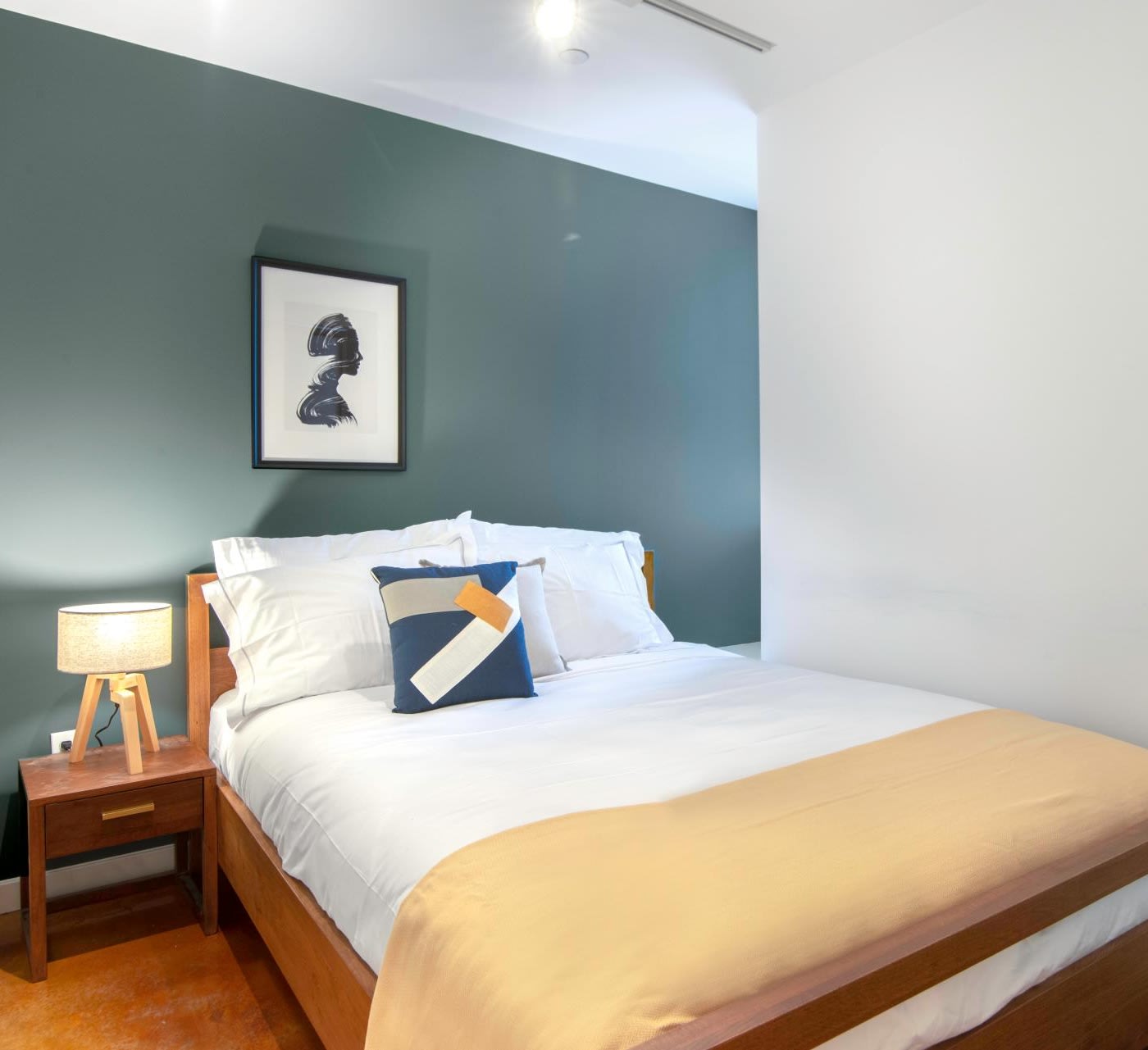 small minimal bedroom with a green accent wall behind the wooden frame bed, small bedside table with a warm lamp