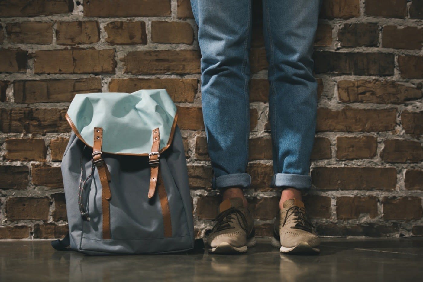 man's feet as he is standing against a brick wall with a backpack on the floor next to him