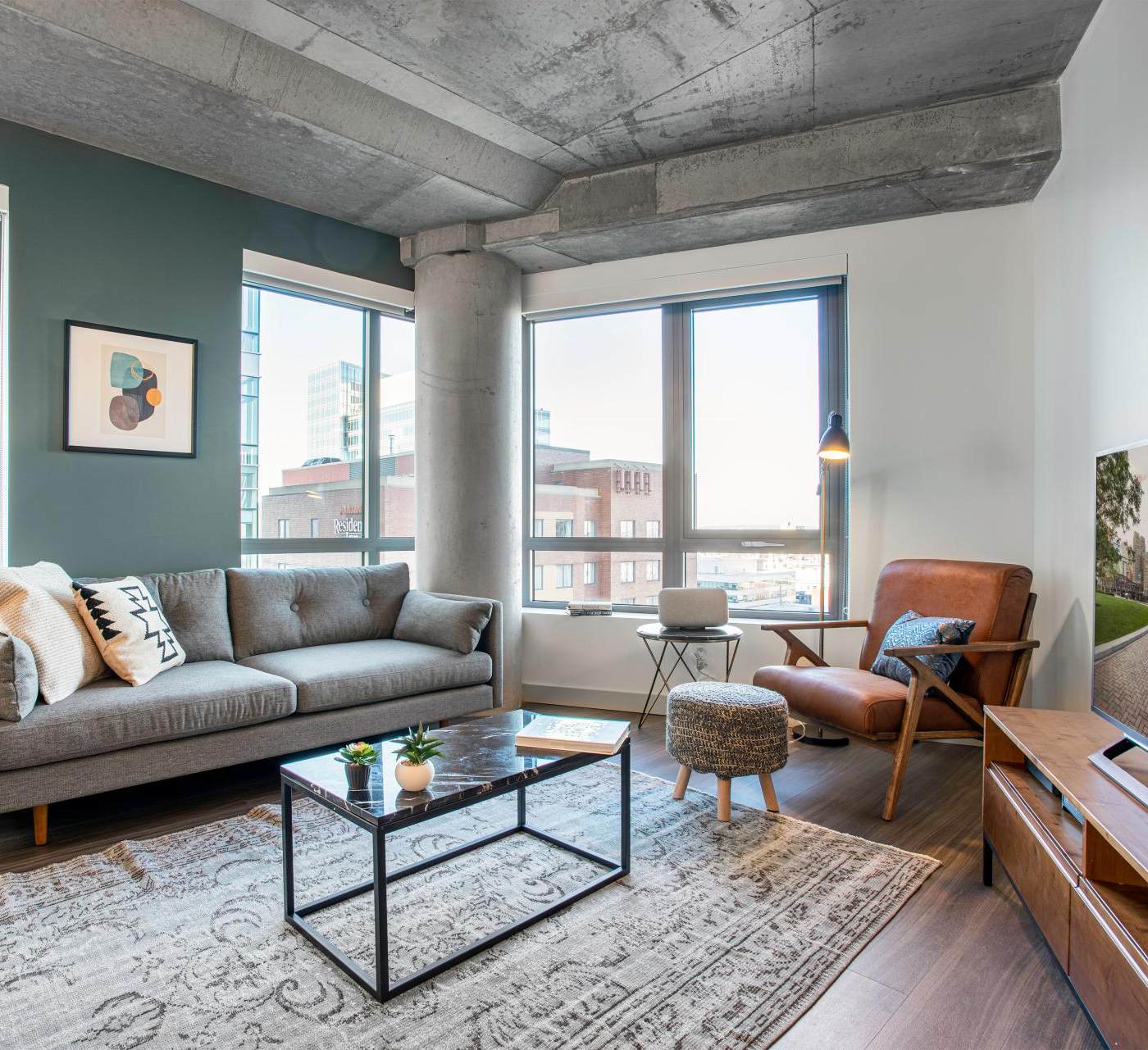 one bedroom apartment living space with cement ceiling and dark marble table and large windows letting natural light in