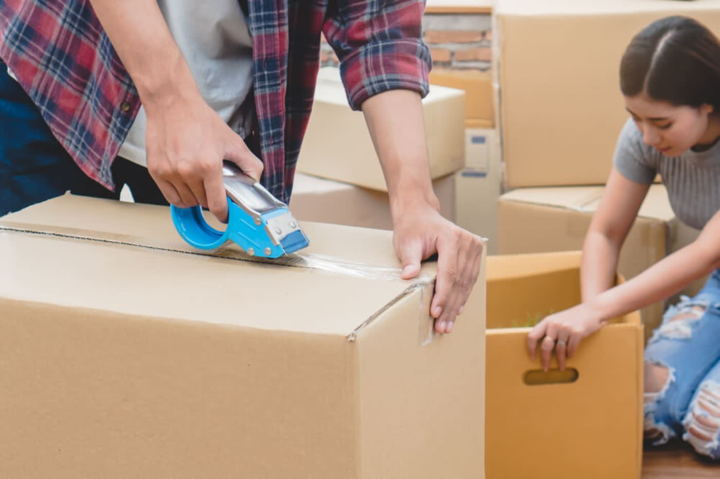 A man is taping up a cardboard box while a girl is packing a cardboard box up with items.
