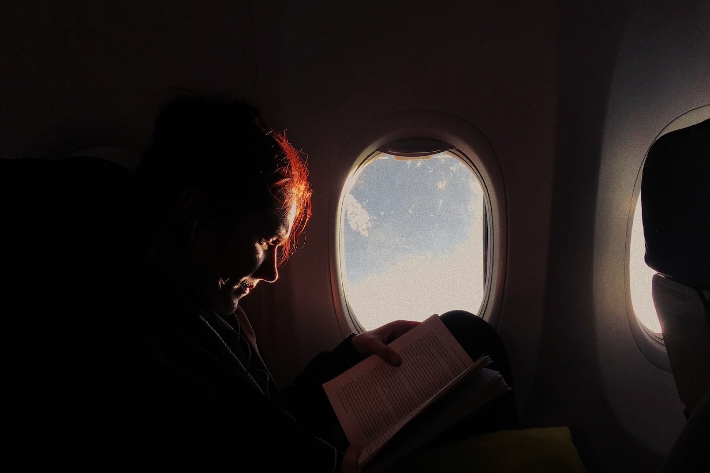woman reading with low lighting on a window airplane seat