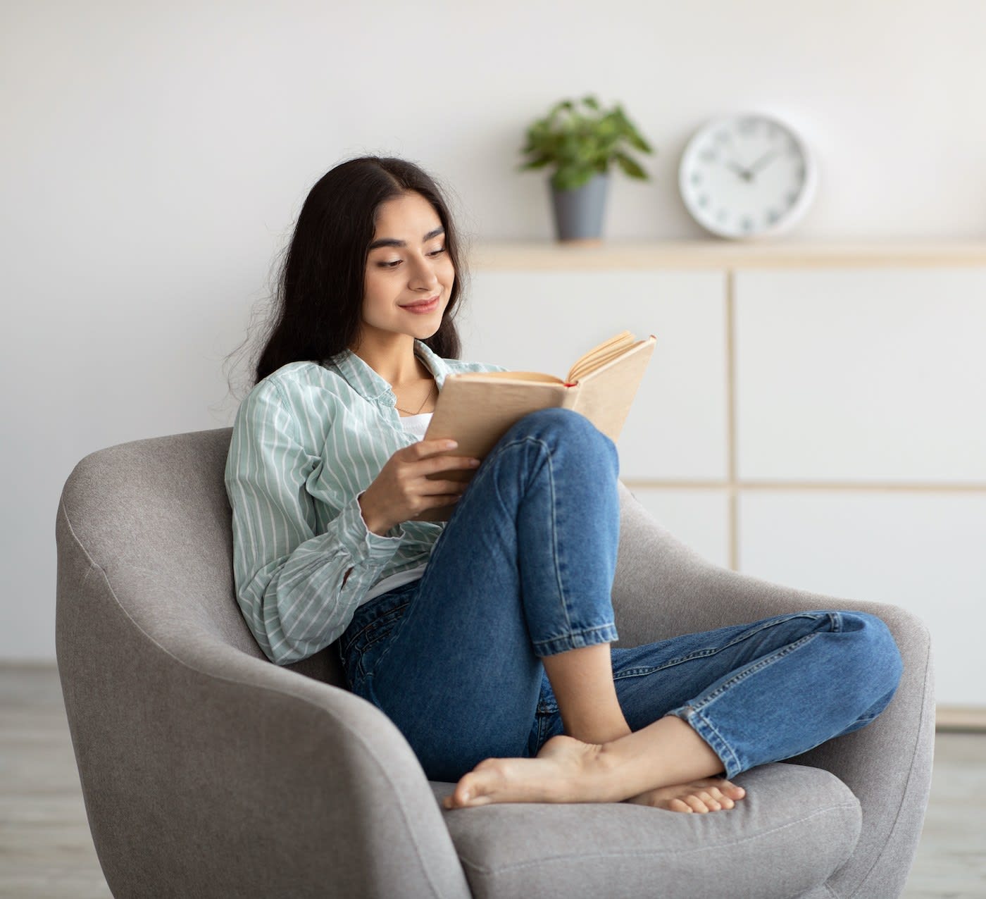 young woman sitting comfortably on an armchair reading a book