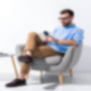 a man is sitting on an armchair looking at his phone