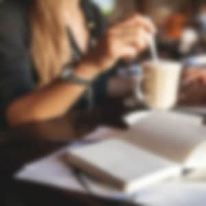 woman sitting a table drinking coffee while working on her laptop