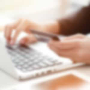 woman holding credit card implying online payment with white laptop