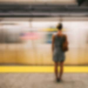 Woman in a grey dress with bare legs standing with her back to the camera, facing a fast moving train