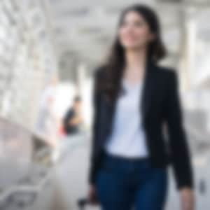 business travel - young woman with hand luggage walking down sidewalk in urban city