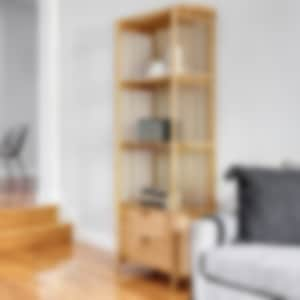 minimal living space, wooden floor, grey couch, wooden shelving unit with very little decor and a small table for two with a muted painting above and a floor lamp next to it