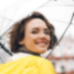 woman smiling, holding an umbrella and wearing a yellow rainjacket