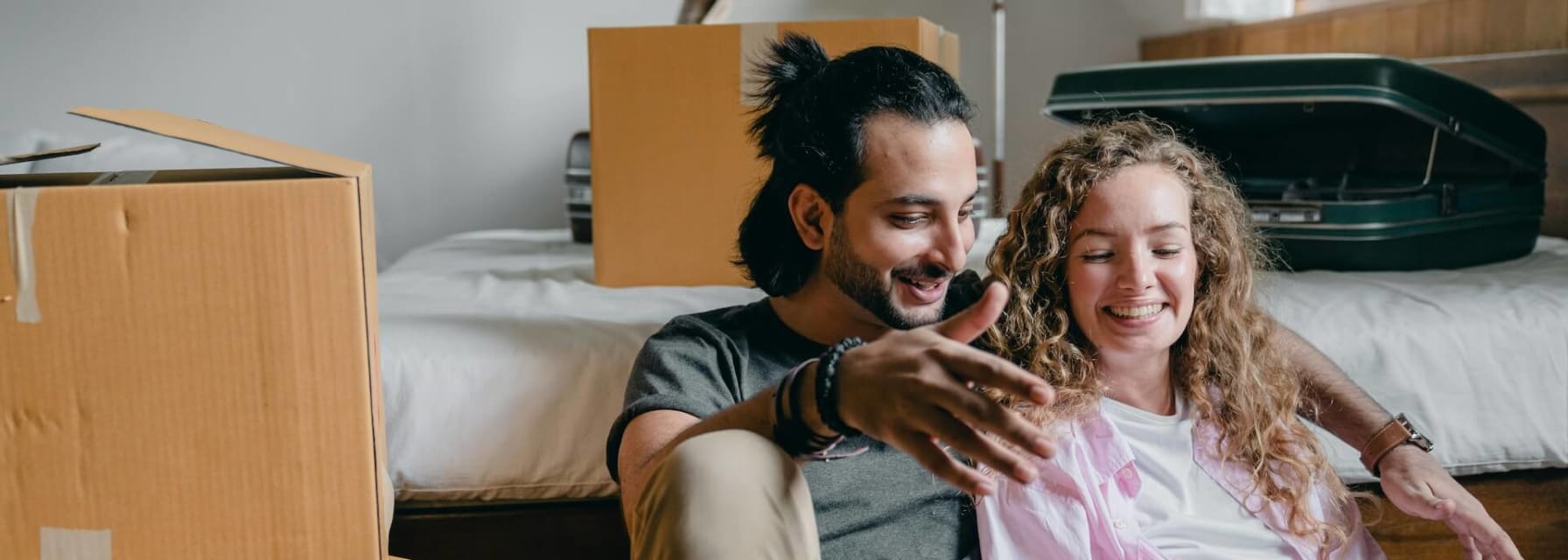 A couple sitting near a bed and moving boxes