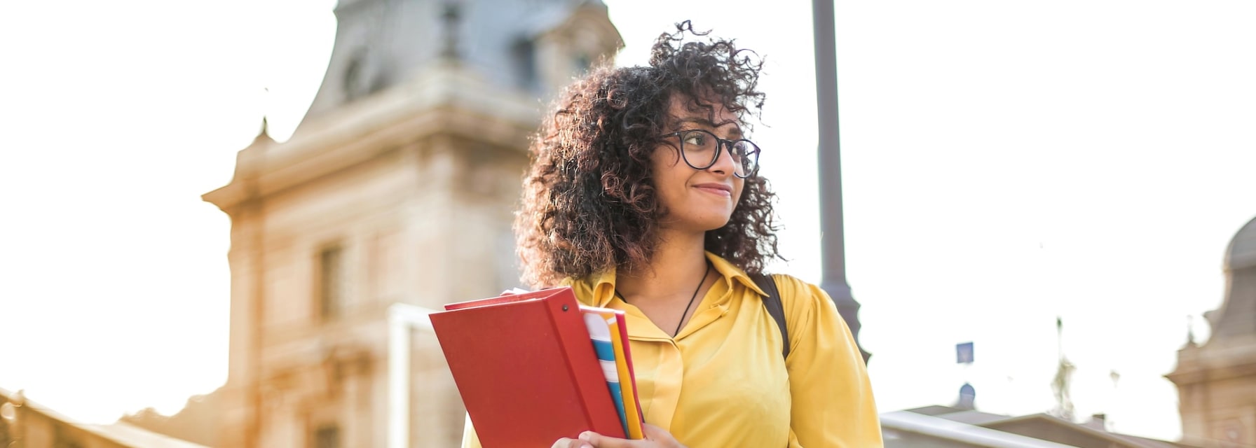 Female student holding books in front of a school building