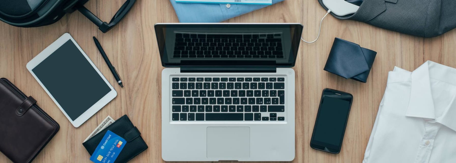 shot from above, showing a table with a laptop, a phone, a small suitcase, some shirts, ties and a couple of wallets