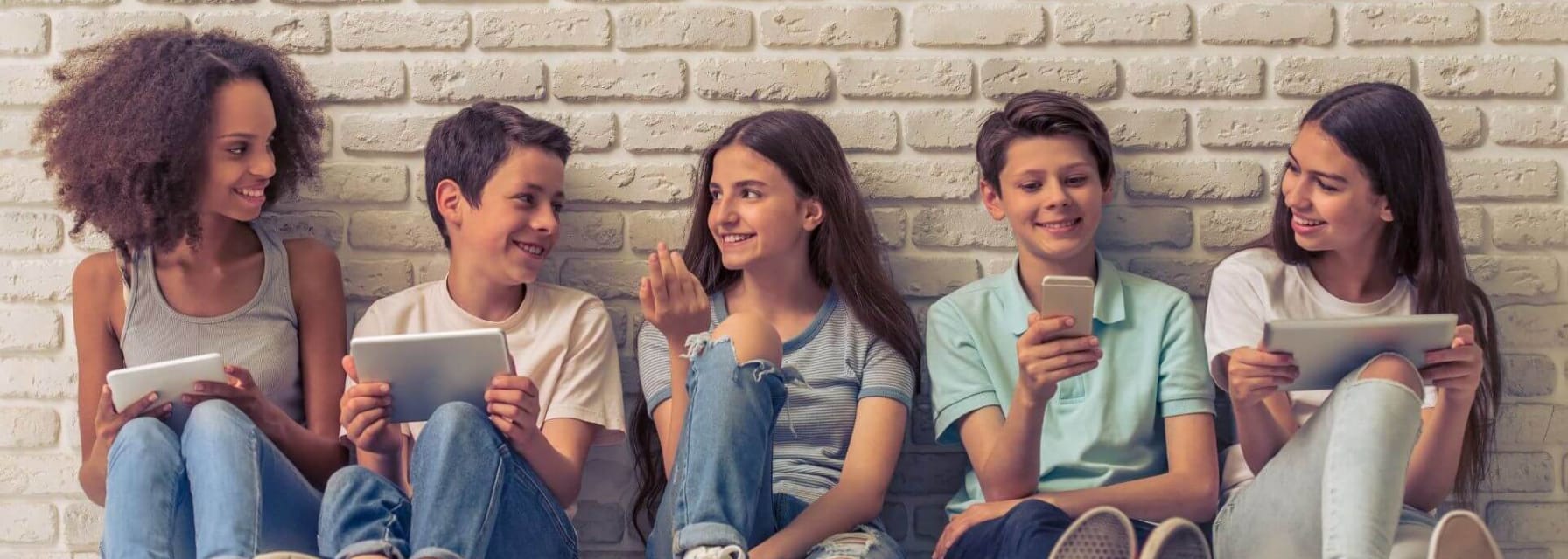 children sitting and looking happy in front of a brick wall