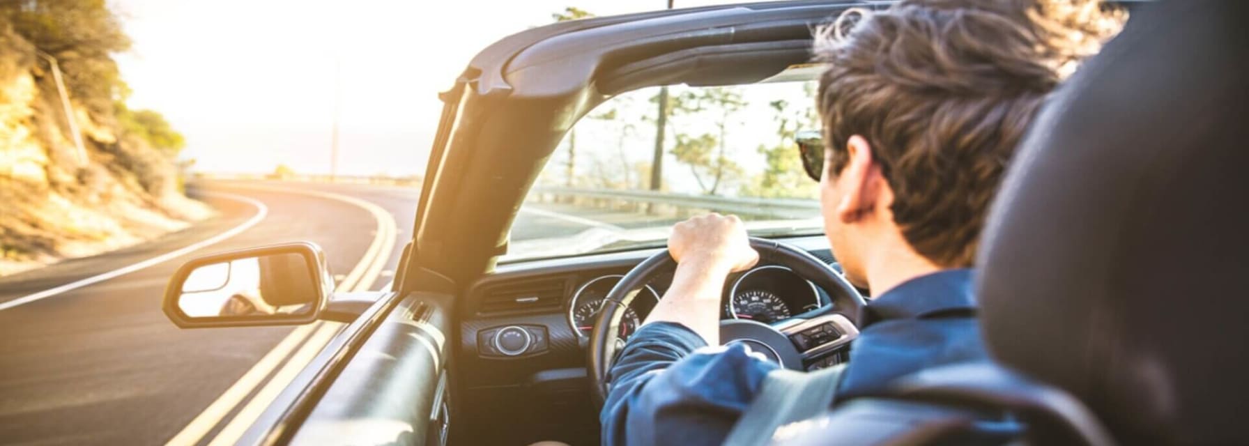 man driving down the road in an open top convertible