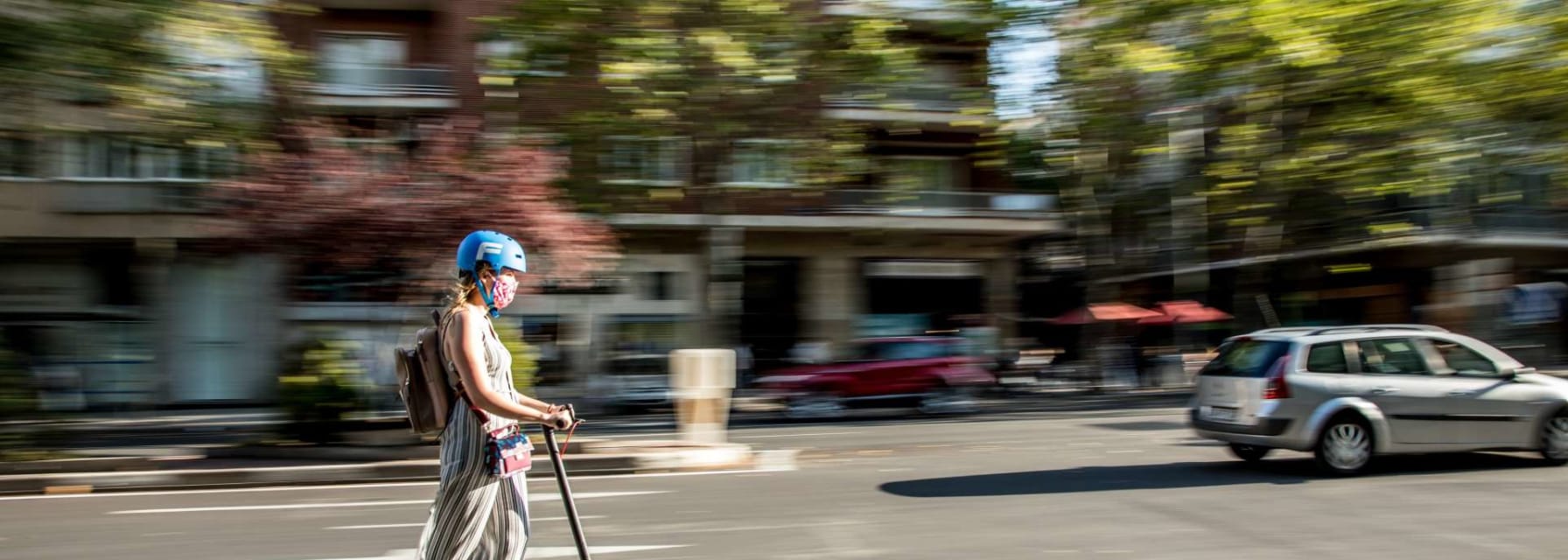 A woman driving a scooter in the middle of a boston road.