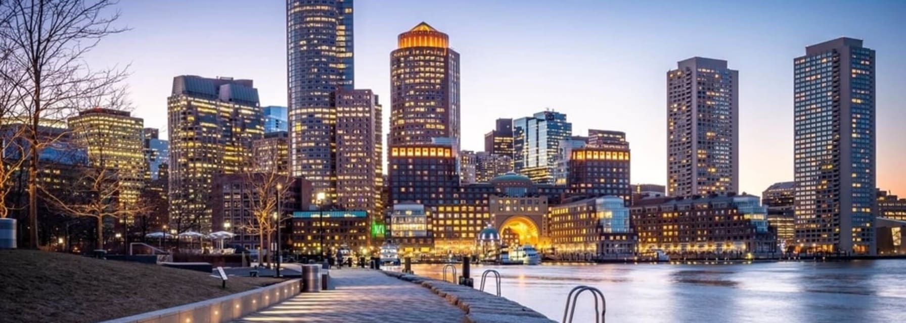 boston city skyline at night with all the buildings lit up and a body of water in the right half of the image