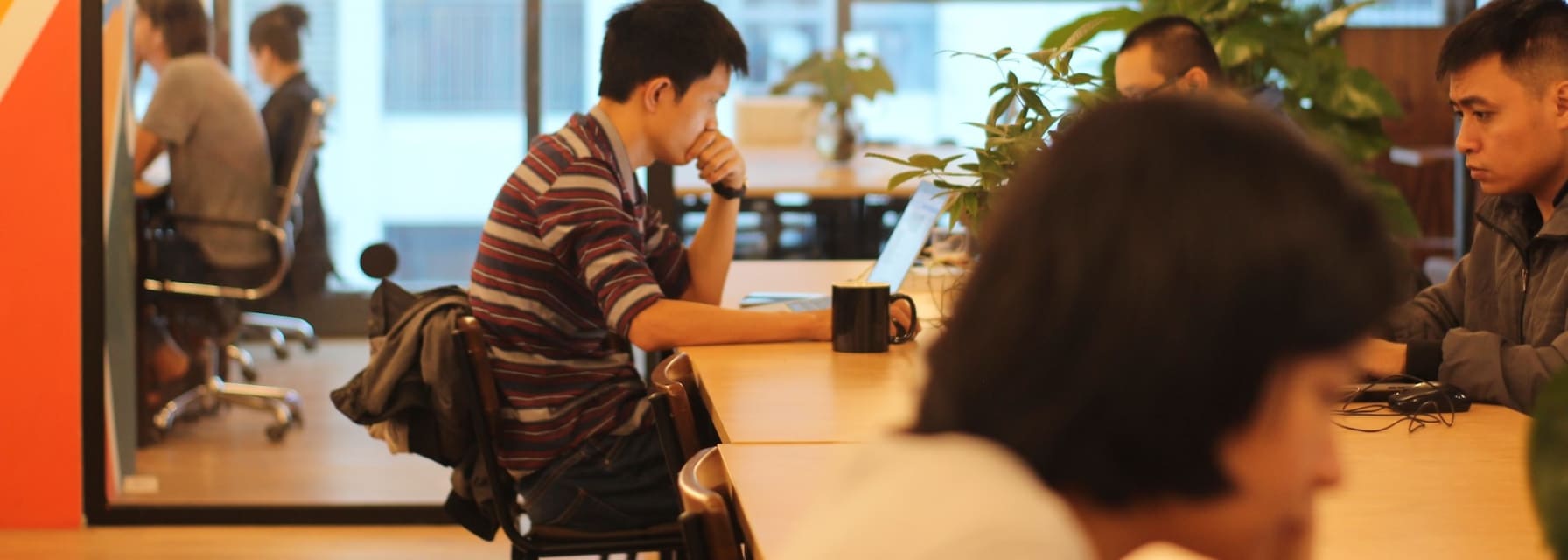 People working in a coworking space with rooms separated by glass walls.