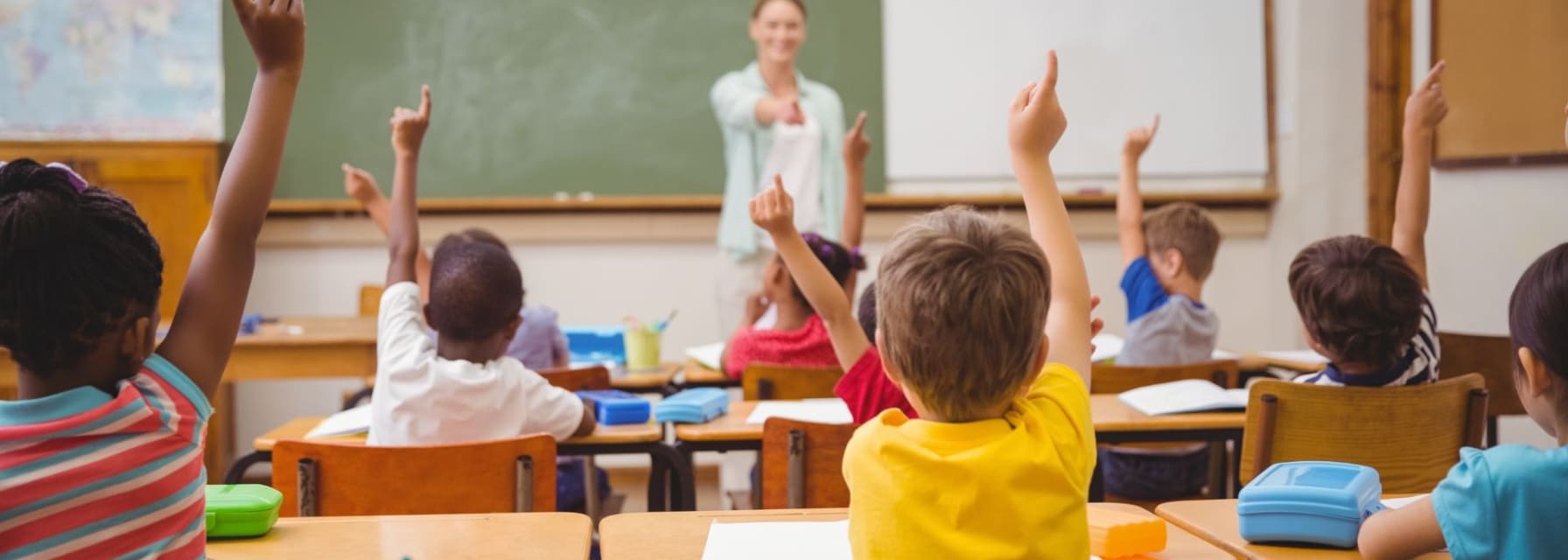 young pupils raising their hands during class teacher pointing at child in yellow