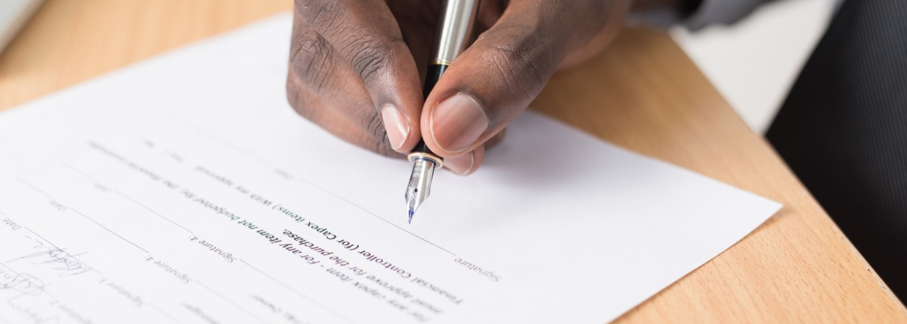 The hand of a man signing a contract with a pen.