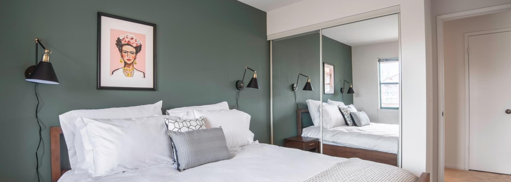 small bedroom with a double bed, a large mirror next to the bed, green accent wall and two nightstands with lamps