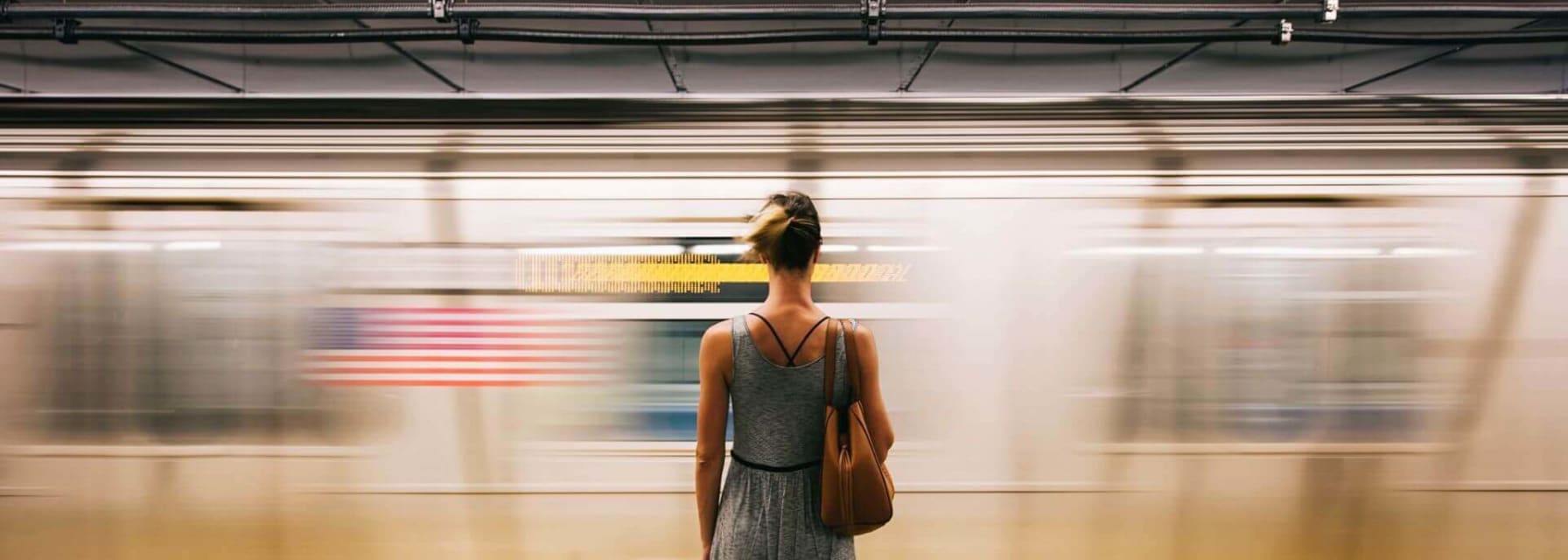 Woman in a grey dress with bare legs standing with her back to the camera, facing a fast moving train