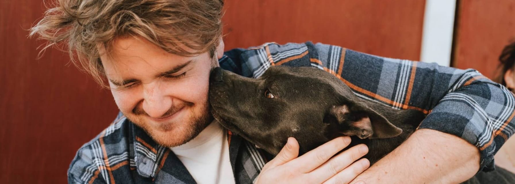 man hugging a Pitbull puppy and it's licking his face