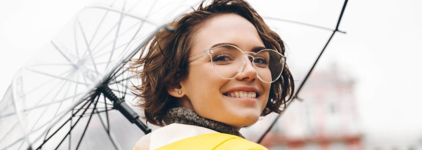 woman smiling, holding an umbrella and wearing a yellow rainjacket