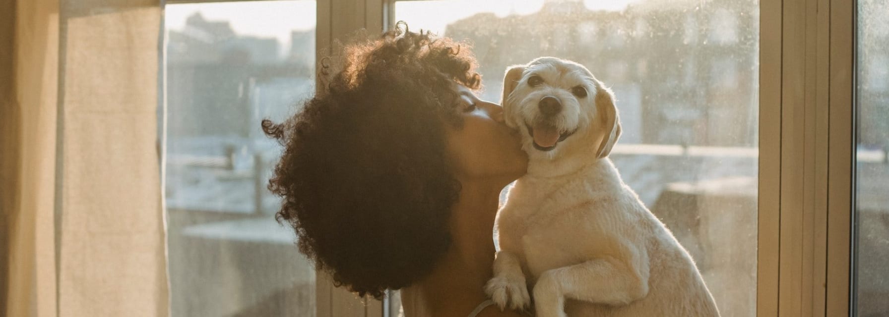 woman hugging her dog and kissing his cheek while he looks at the camera smiling