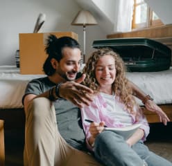 A couple sitting near a bed and moving boxes